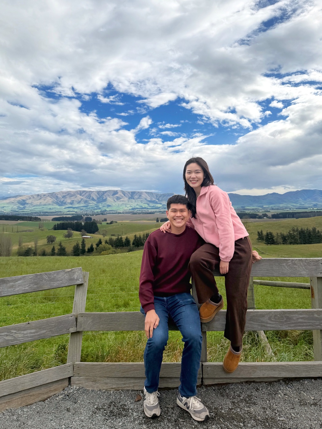 Gabriel and Estella sitting by a fence with green hills behind them